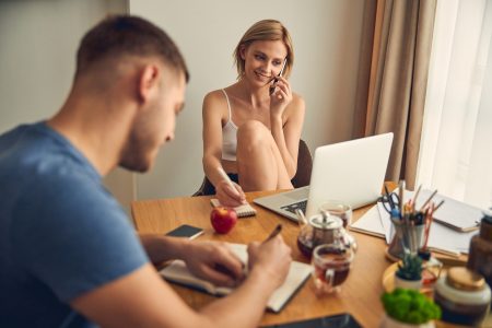 Śliczna blond dama spędza czas rozmawiając przez telefon w pobliżu laptopa, podczas gdy brunetka mężczyzna pisze w notatniku