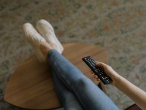 Comfortable home setting with woman lounging and using remote control.
