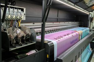 Wydruk próbny w pracy projektanta – jak trafić w kolor i nie przepalić budżetu na materiały A large industrial printer feeding a long pink banner with printed text