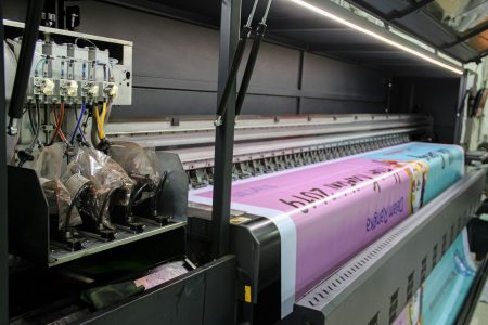 Wydruk próbny w pracy projektanta – jak trafić w kolor i nie przepalić budżetu na materiały A large industrial printer feeding a long pink banner with printed text